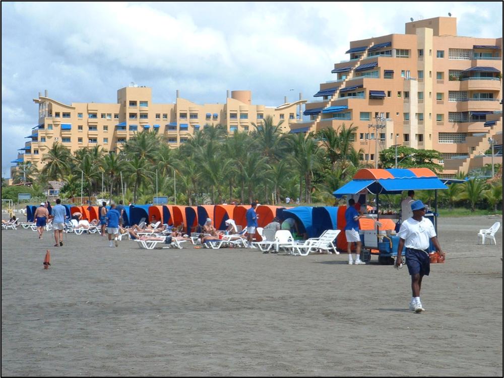 A photograph of a beach front with banana chairs and resort buildings in the background.