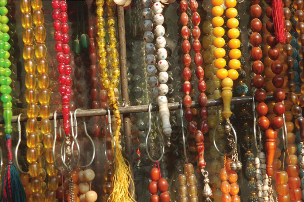 Close-up photograph of strings of coloured prayer beads hanging on a wooden rack.