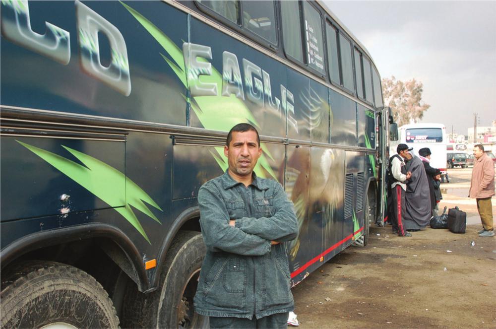 Photograph of a man in a dark blue jacket, standing in front of a black and green bus.