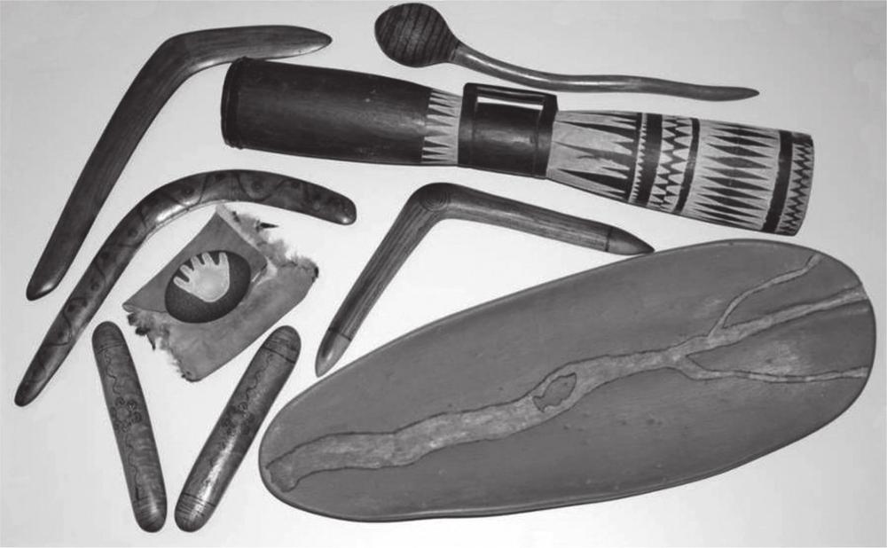 A black and white photograph of three boomerangs, two sticks, a shield and two other objects.