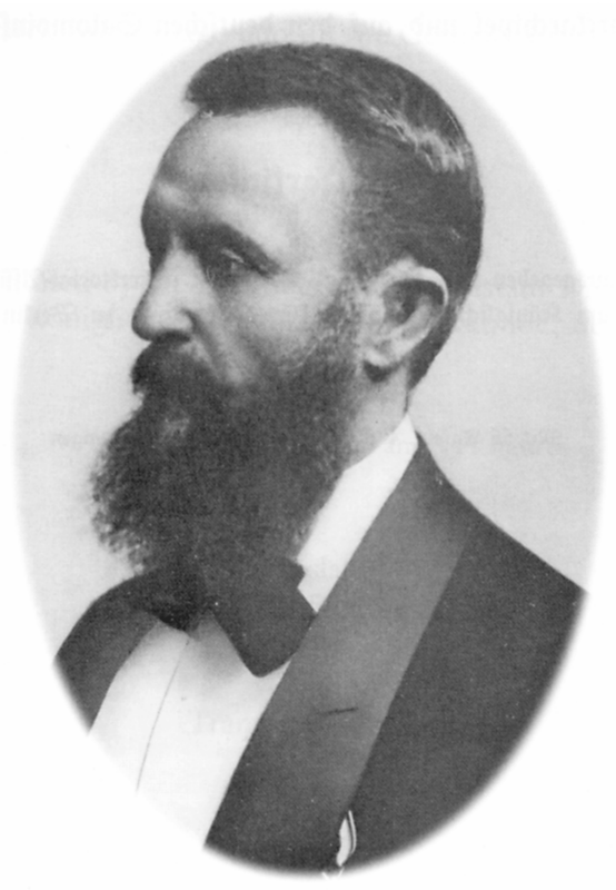 Black and white portrait image of a man with a beard in a suit.