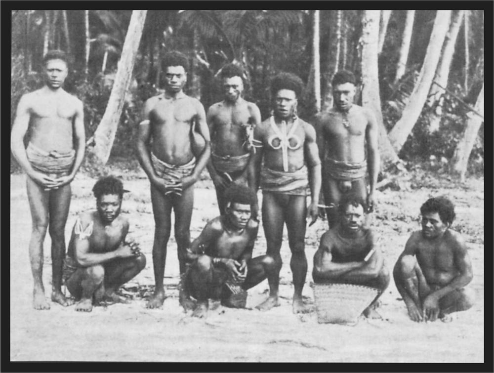 A group of men sitting and standing on the beach of the Arawa Island. There are palm trees in the background.