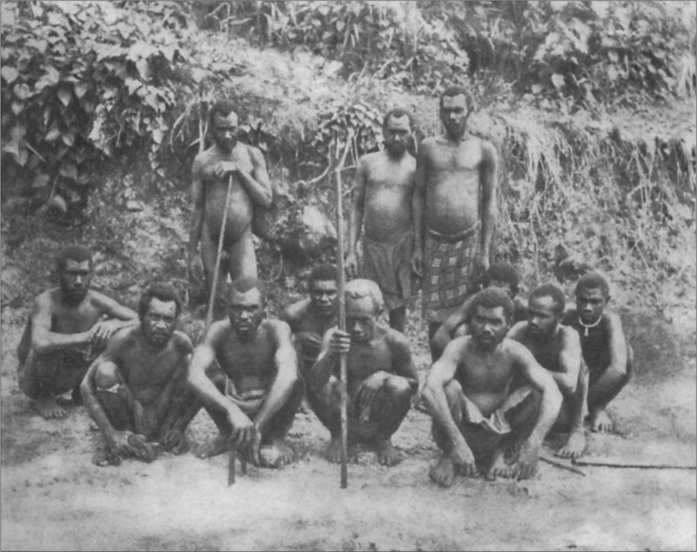 Black and white image of a group of men posing for the camera, many with spears.