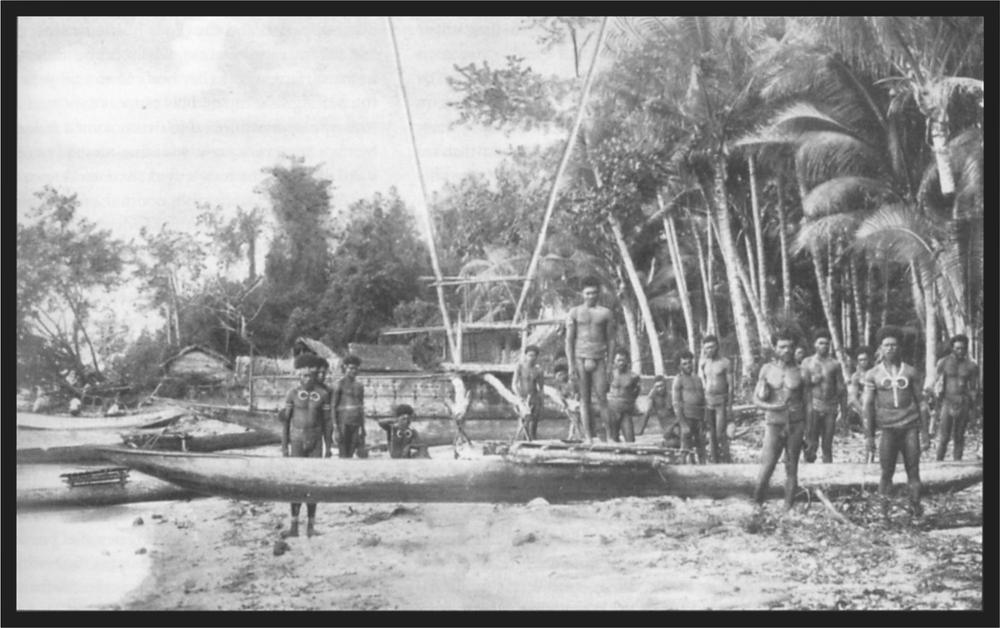 Black and white image of a group of men around long boats on the beach with palm trees in the background.