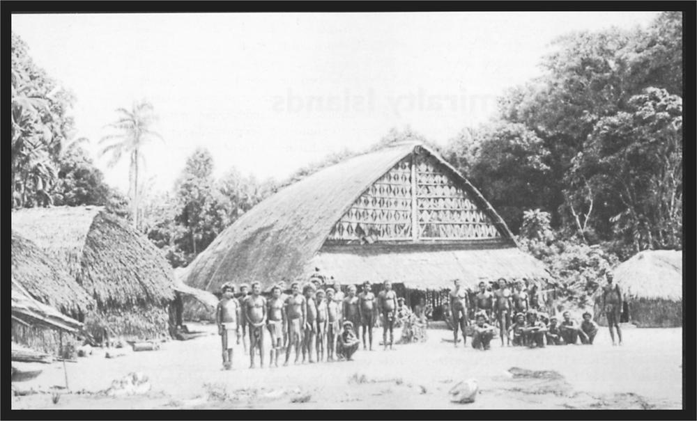 Black and white image of a group of men standing in front of a large hut.