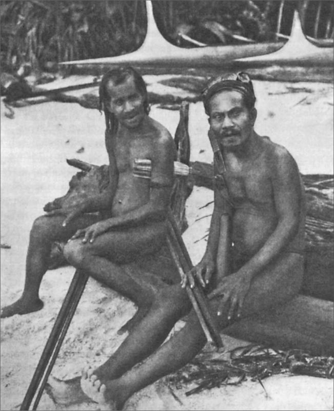 Black and white image of two men sitting on logs on the beach of an island.