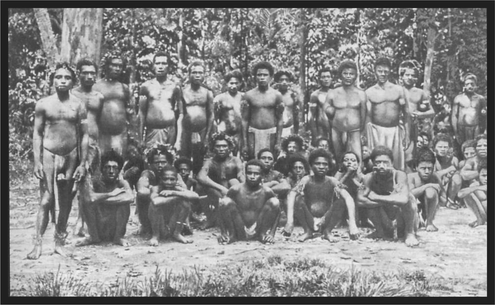 Black and white image of a group of men standing and sitting in front of the trees, many with spears.