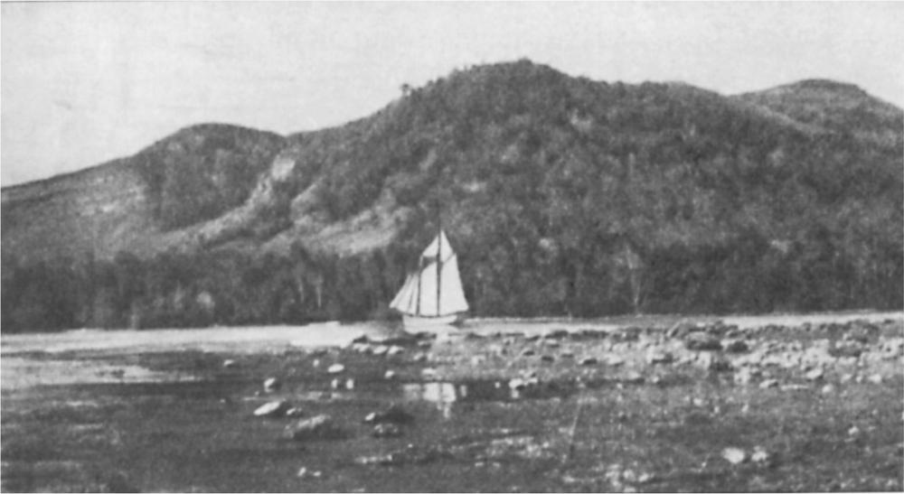 Black and white image of a sail boat on the water with a raised island in the background.