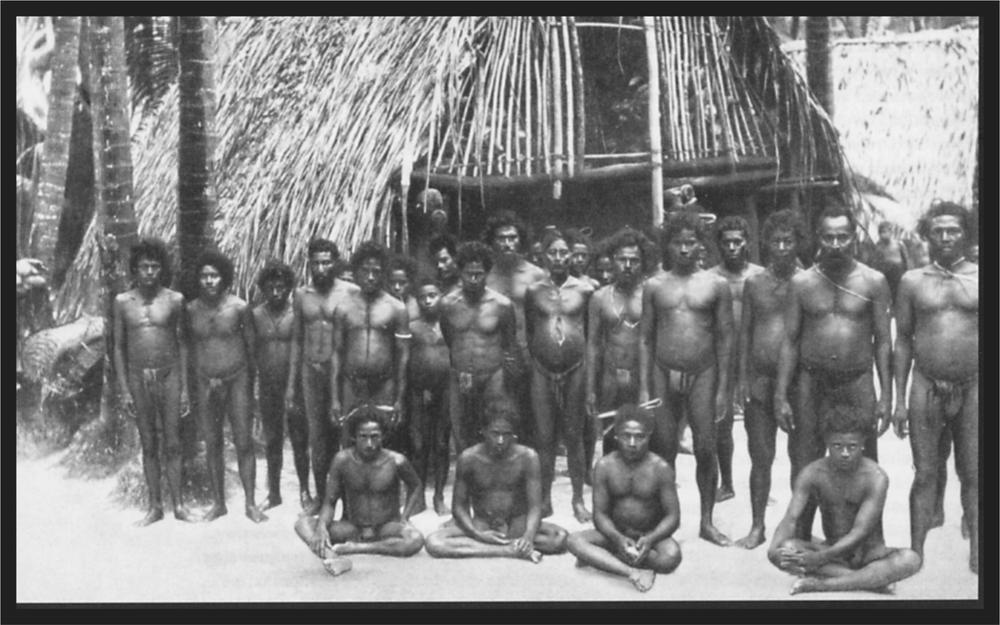 Black and white image of a group of men standing in front of a hut.