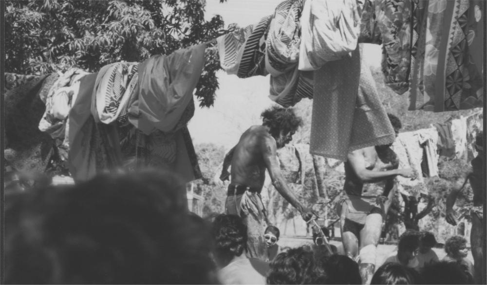 A black and white image of Anoriginal dancers in the middle of a seated crowd.