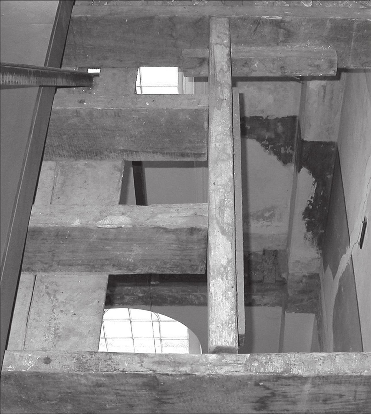 A black and white photograph of a floor cavity revealing a window and peeling paint on the level below.