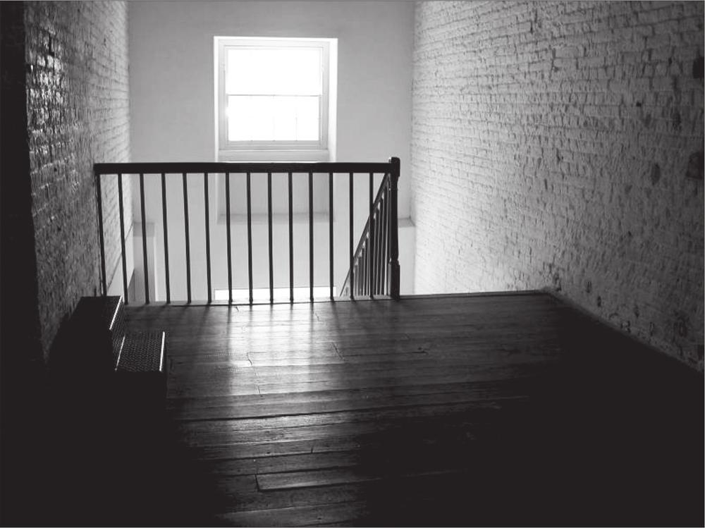 A black and white photograph of a landing on level 3. Light is coming through a window above the landing.