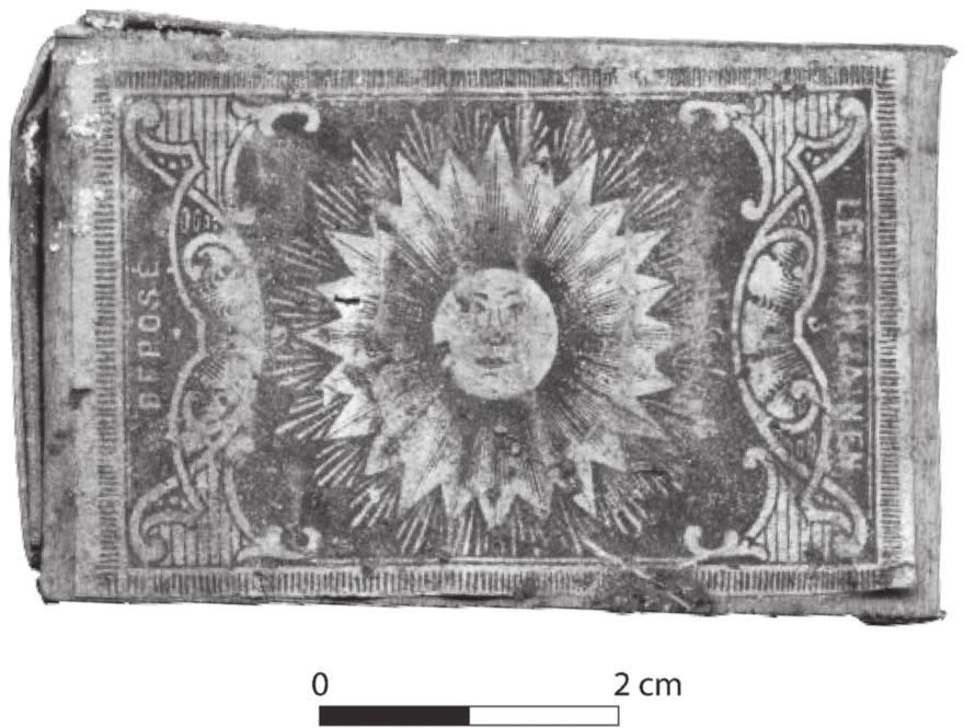 A black and white photograph a matchbox with a smiling sun at the centre.