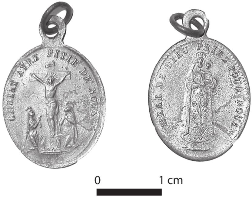 A black and white photograph showing the faces of a medal. One face shows the crucifixion of Jesus and the other shows Mary holding the baby.