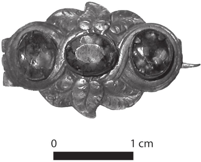 A black and white photograph of a brass brooch with three oval gems and leaves carved around it.