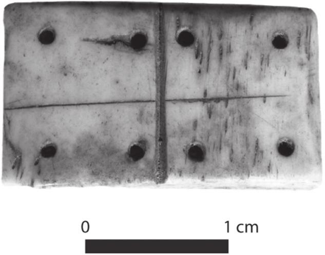 A black and white photograph of a bone domino showing eight dots.