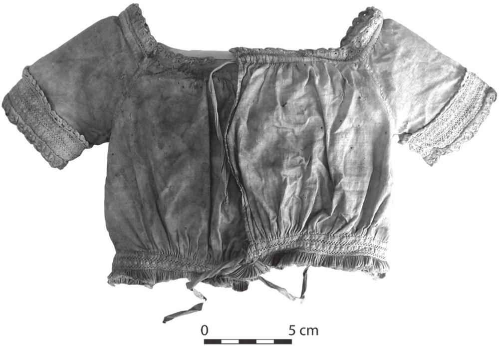 A black and white photograph of a small bodice with decorated bands along the sleeves, waist and neck.